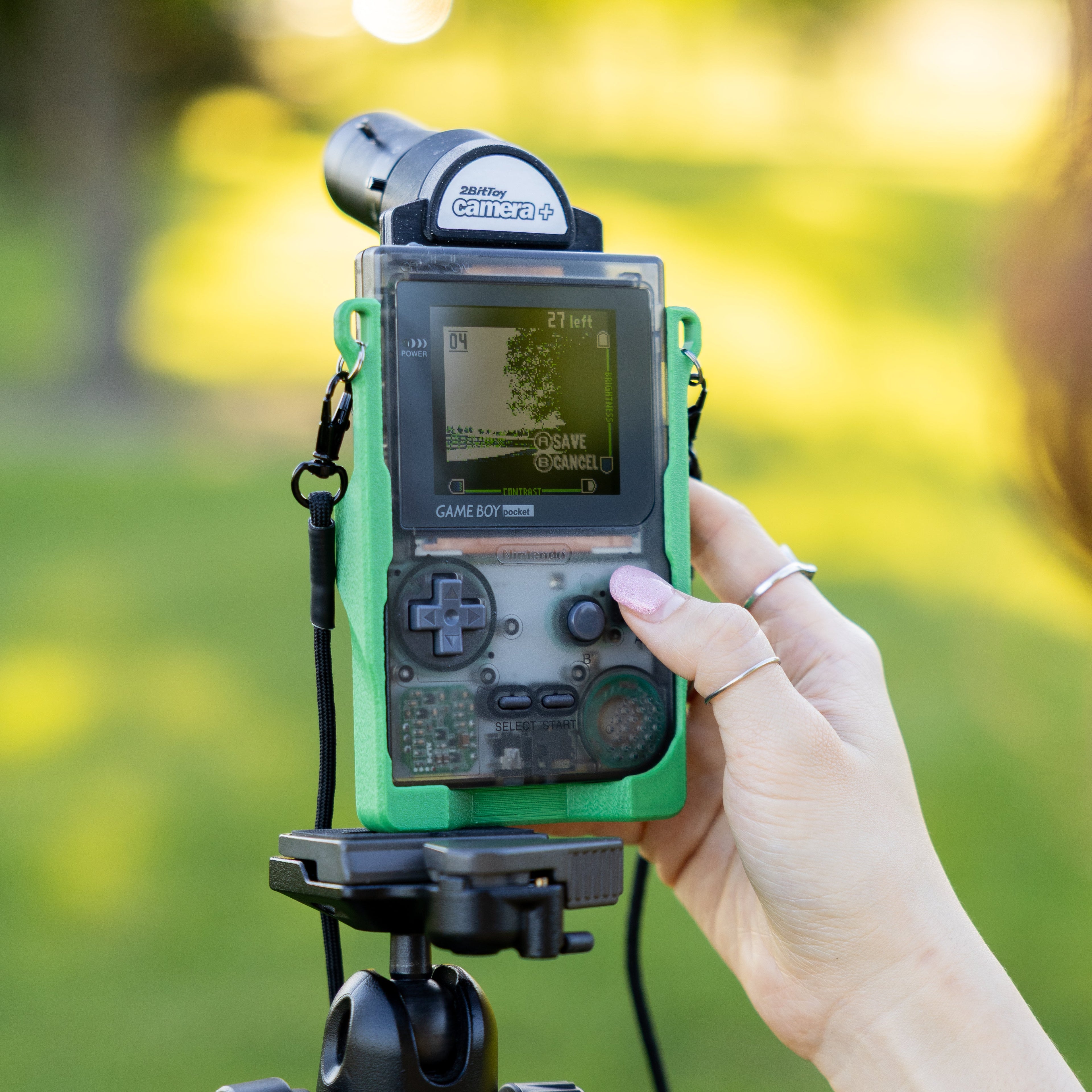 Hand holding a vintage Game Boy on a tripod with a blurred natural background