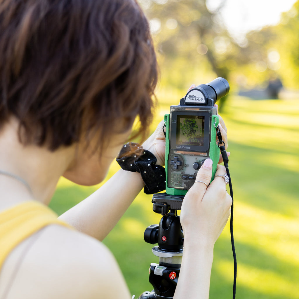 Close-up of a Game Boy Pocket screen showing a live camera feed outdoors at a park.