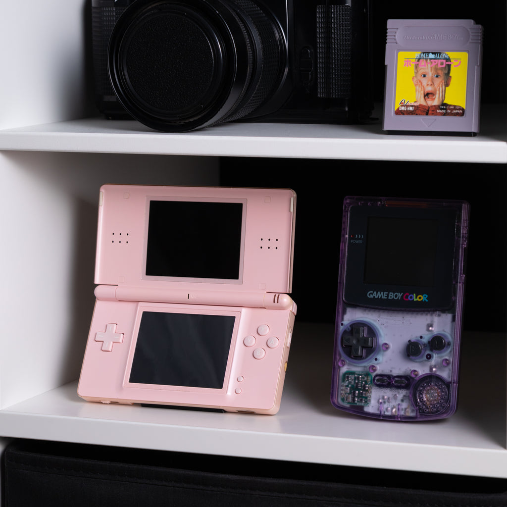 Lifestyle shot of a curated retro collection with a DS Lite, vintage film camera, and a Japanese Game Boy game.