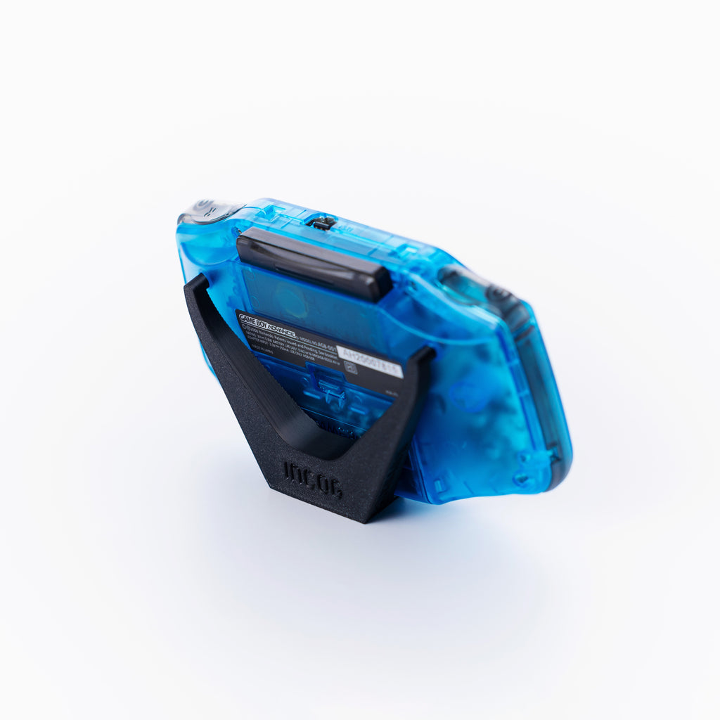 A translucent blue gameboy advance using a black INCOG display stand shown from an angle on an off white background.