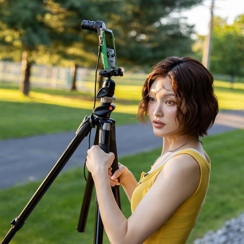 Side profile of a woman holding a Game Boy Pocket with a 3D-printed tripod carrier accessory.