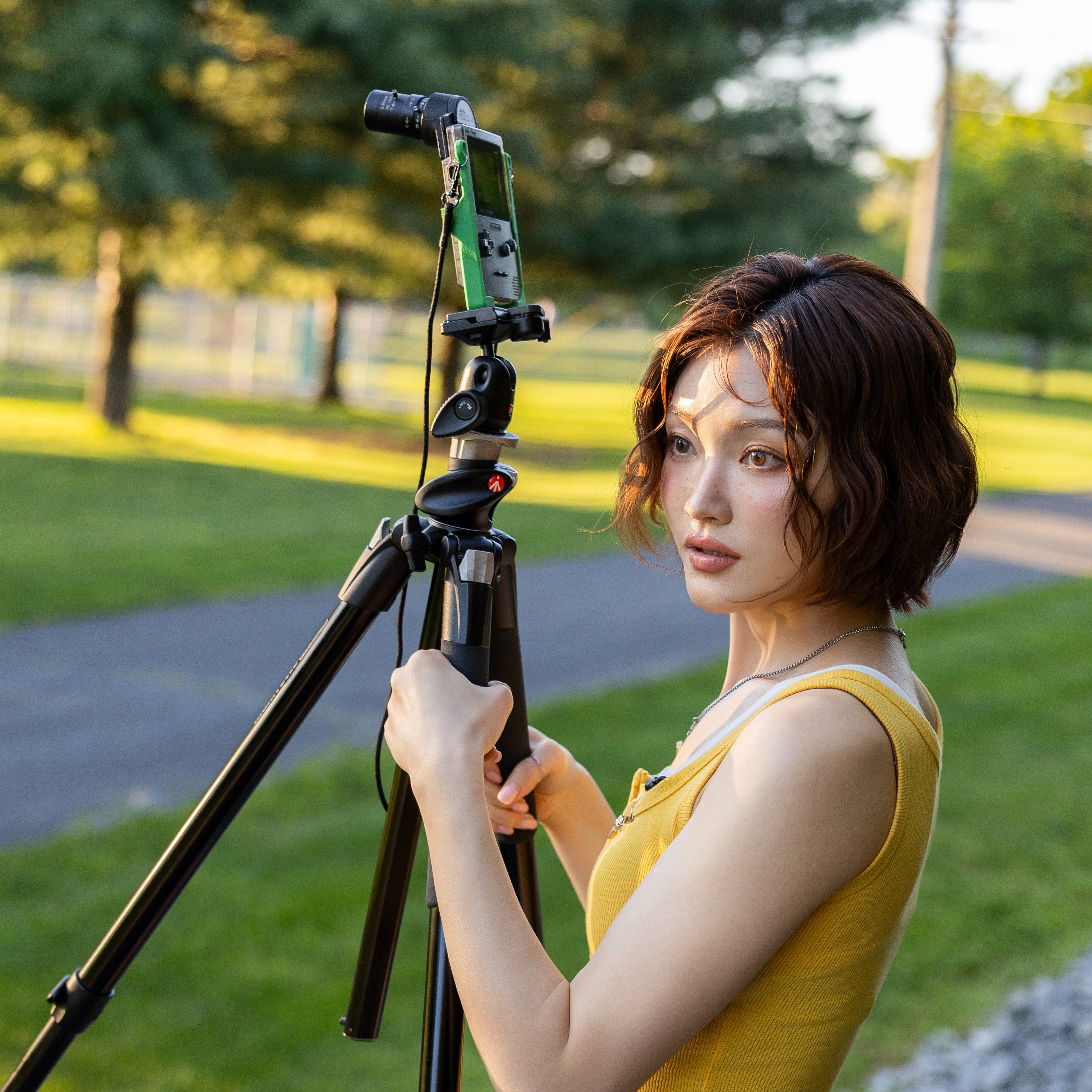 Side profile of a woman holding a Game Boy Pocket with a 3D-printed tripod carrier accessory.