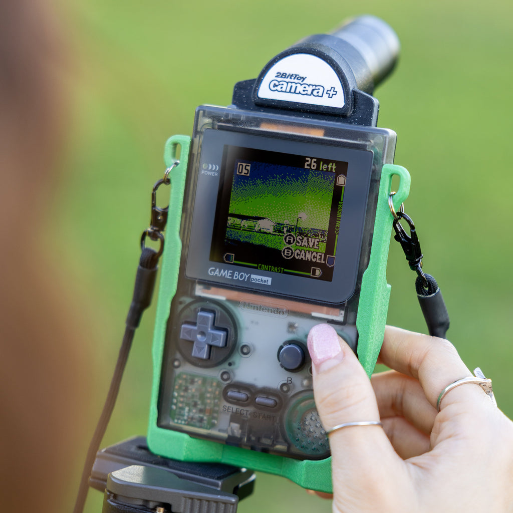 A pixelated photo being captured on a Game Boy Pocket screen, held in a custom carrier.