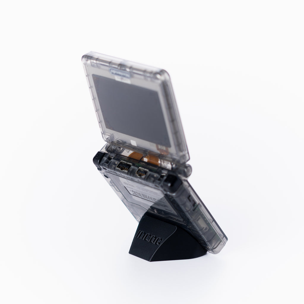 A translucent black game boy advance sp console standing open on a black INCOG display stand, photographed against a clean off white background.