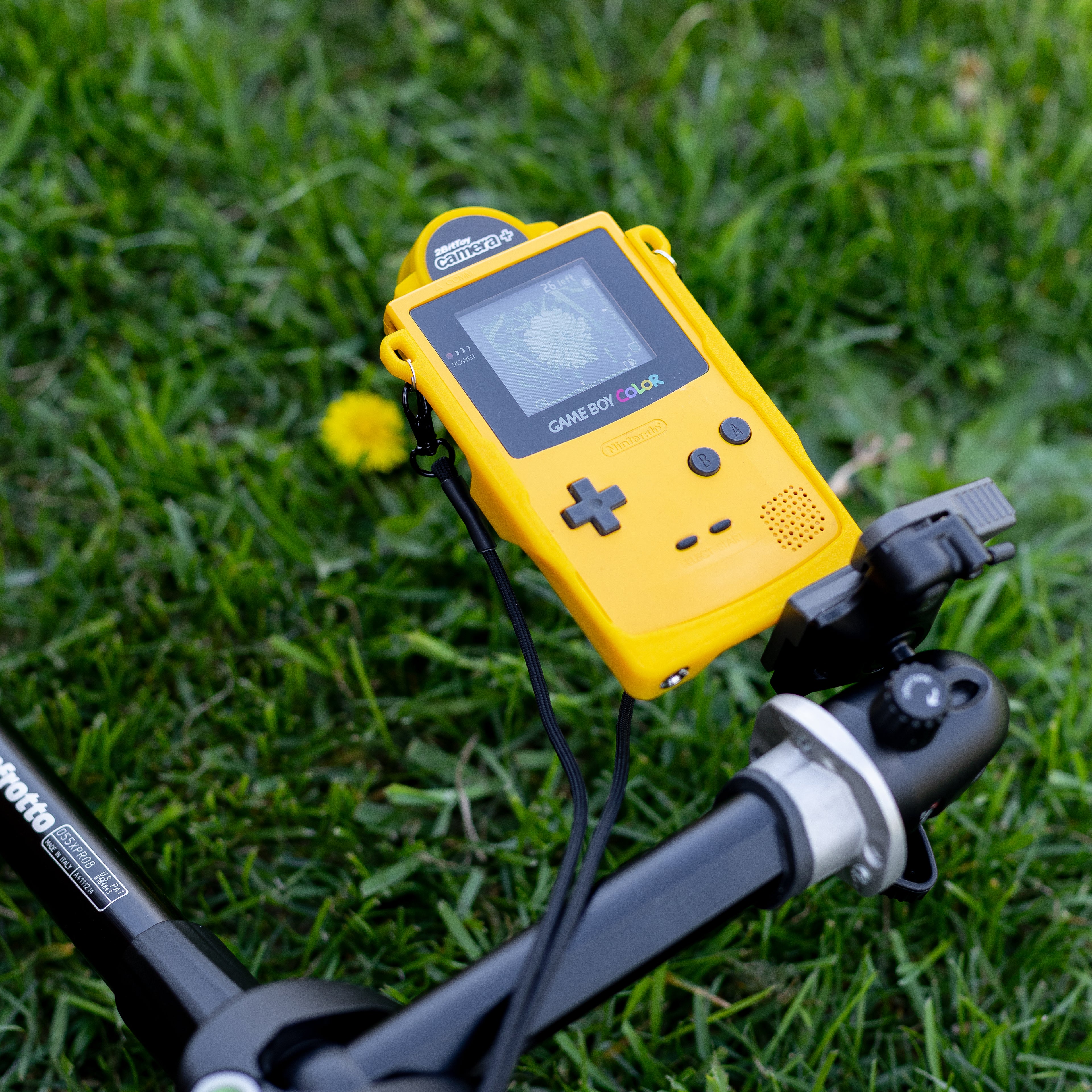 Low-angle outdoor shot of a yellow Game Boy camera setup on a tripod, highlighting the rugged ABS plastic Cradle