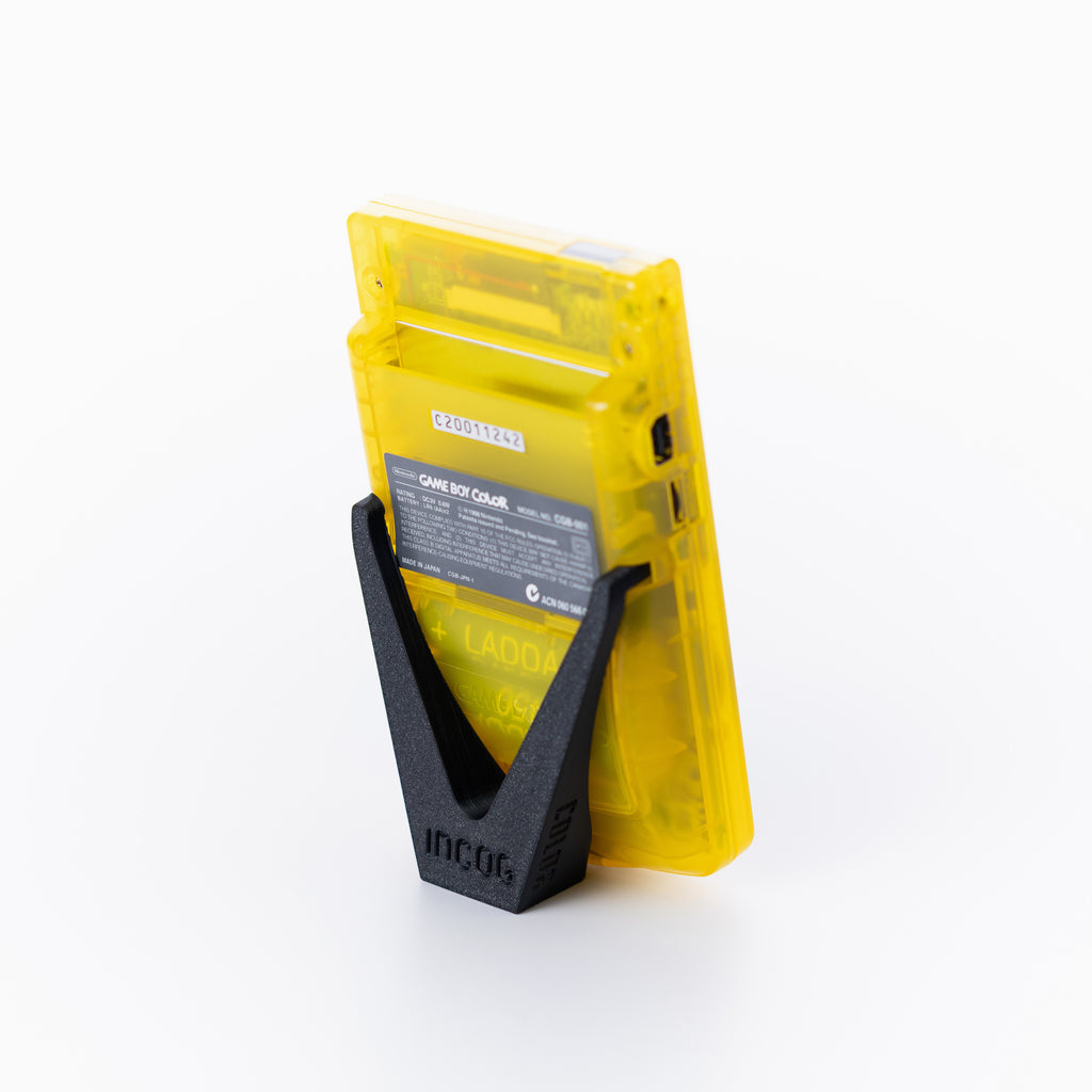 A translucent yellow gameboy color using an INCOG display stand, photographed on a clean off white background.
