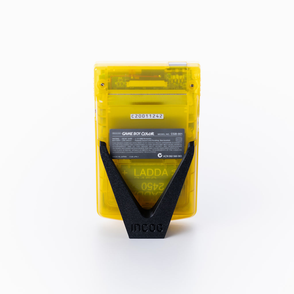 A translucent yellow Game Boy Color shown from the back using an INCOG display stand on an off white background.
